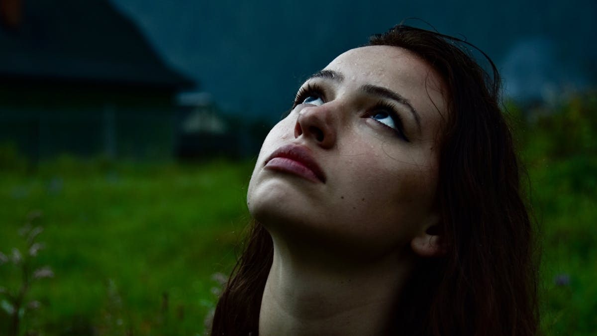Close-up of a woman looking upwards during a rainy day, evoking contemplation.